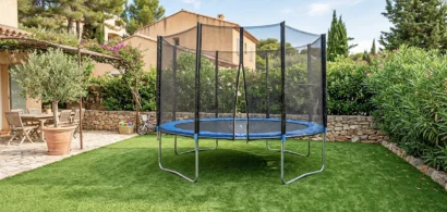 Trampoline à filet posé sur une pelouse synthétique dans un jardin